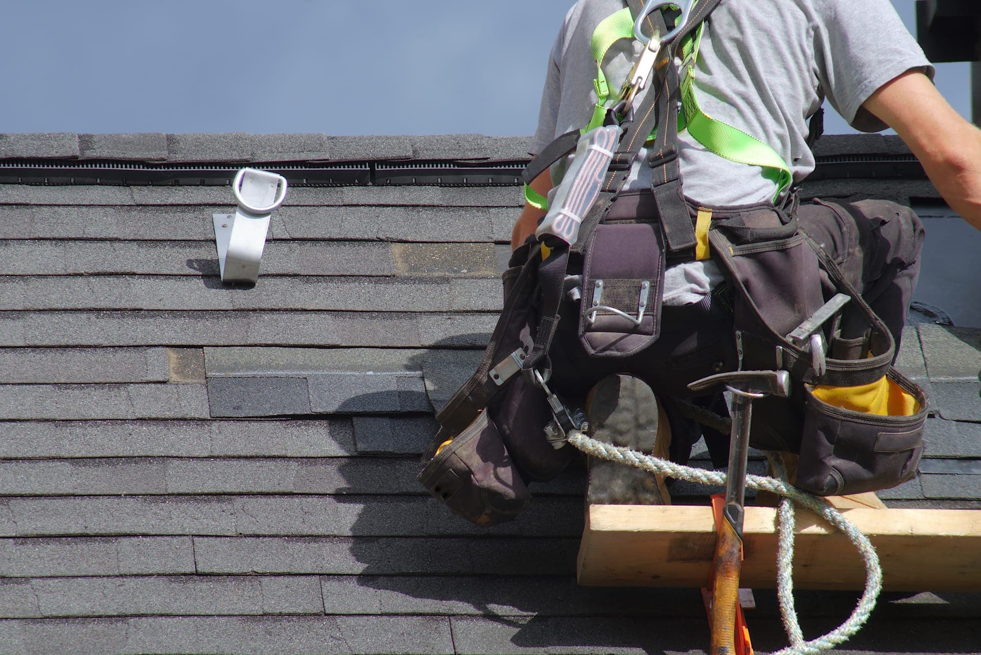 Roofer in safety harness working on asphalt shingles